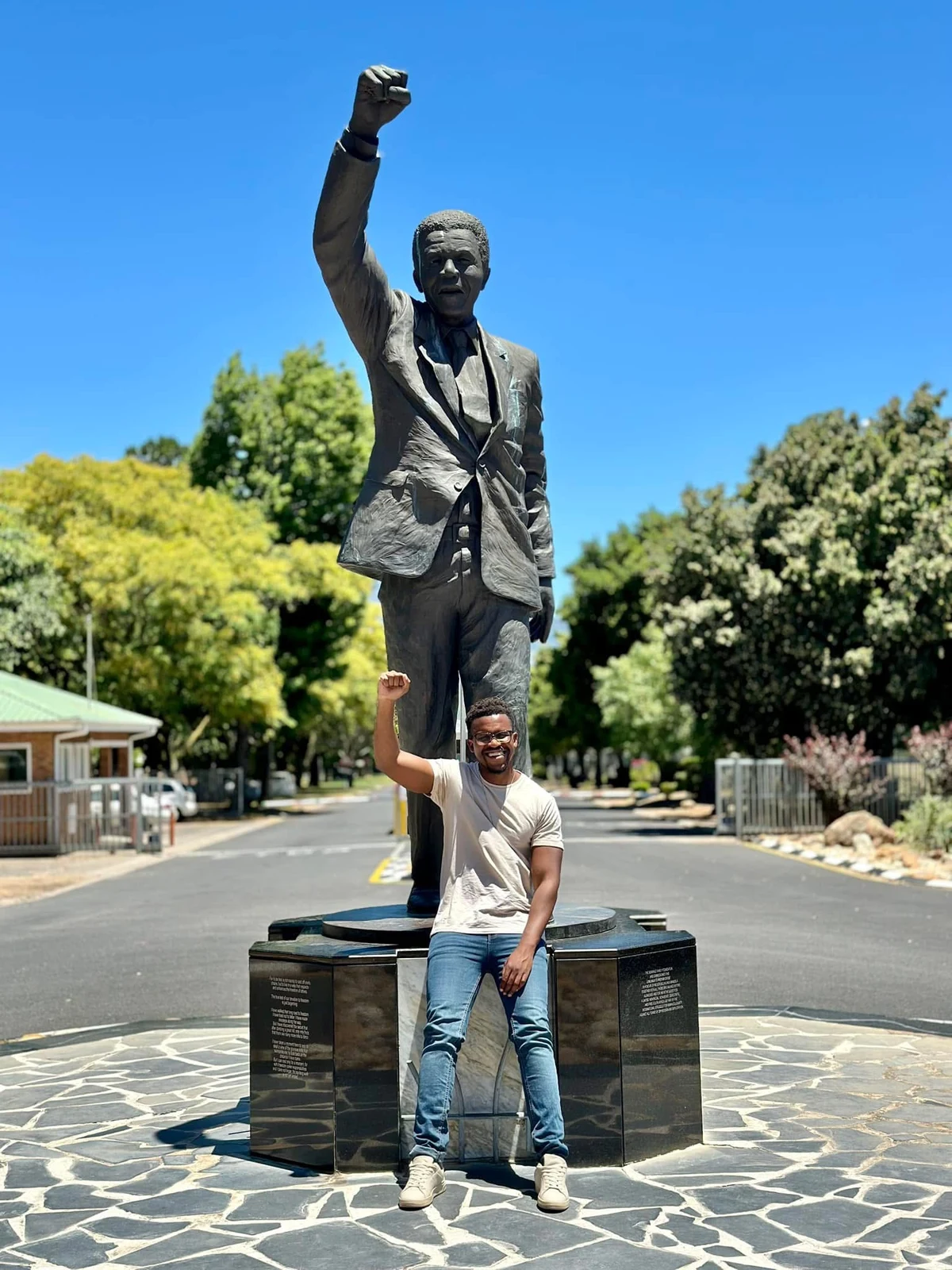 Phinius standing beside a statue of Nelson Mandela, with a raised fist.