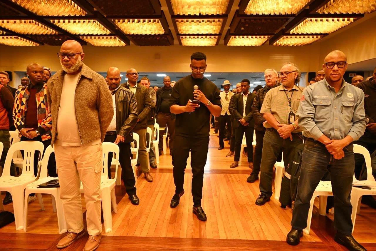 Phinius standing alongside participants gathered in a hall.