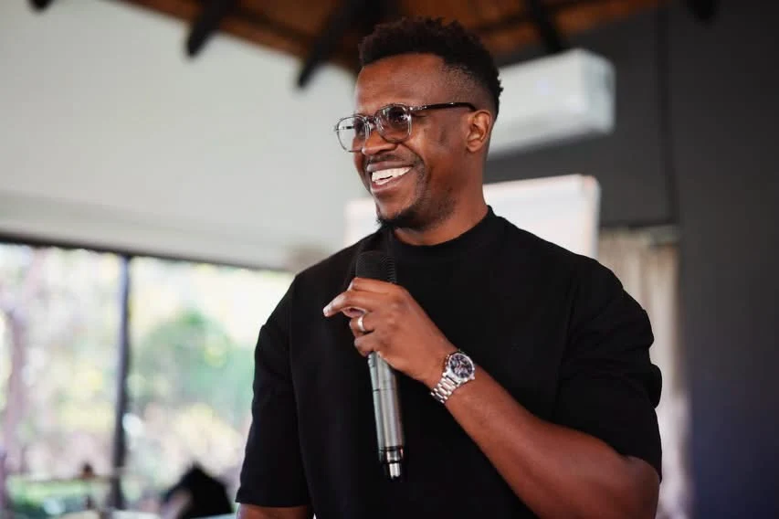 Phinius Sebatsane smiling while speaking with a handheld microphone.