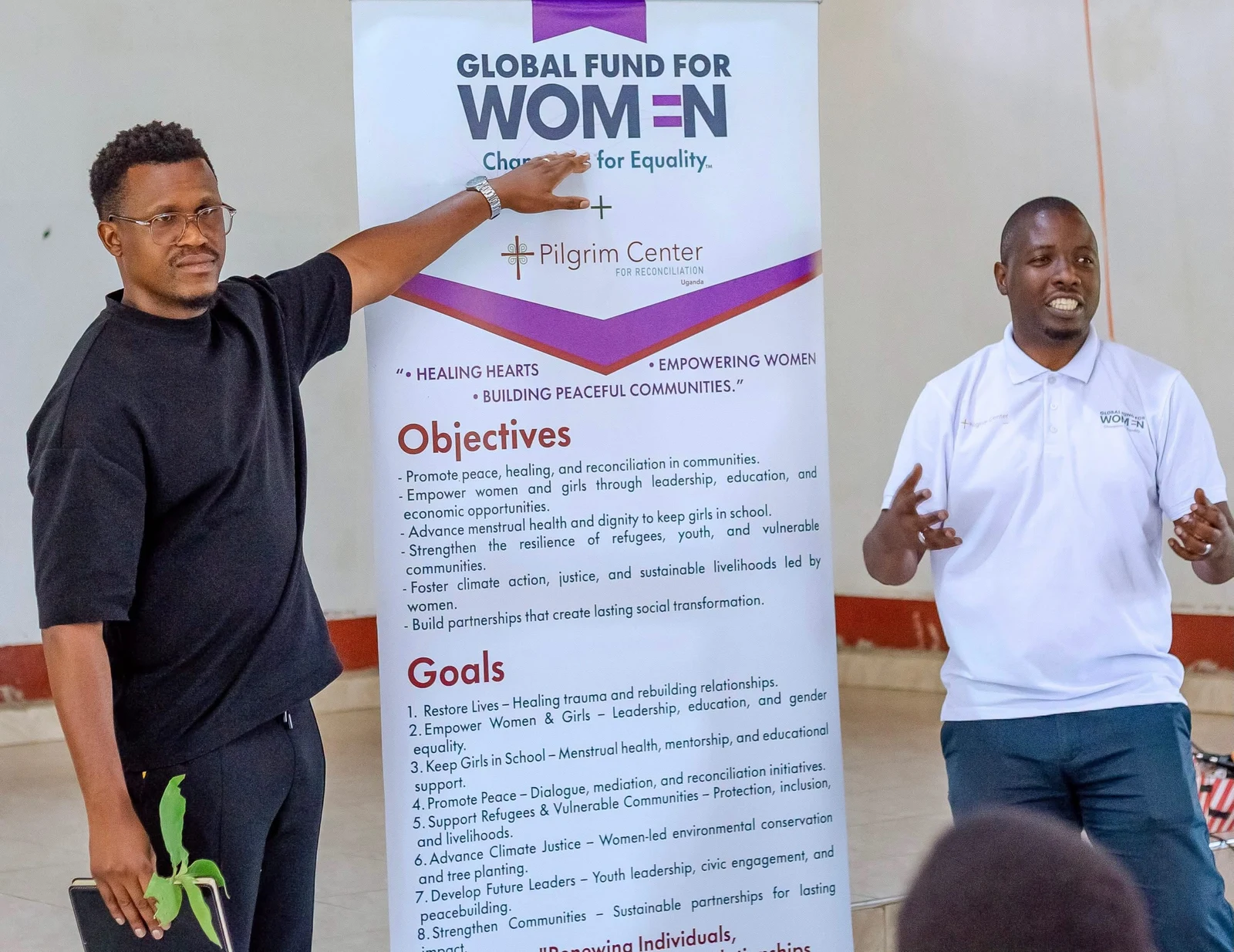 Phinius and a fellow speaker beside a banner about building peaceful communities.